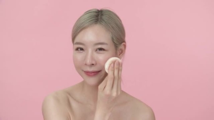 美丽的亚洲女人在脸上化妆粉扑的肖像。