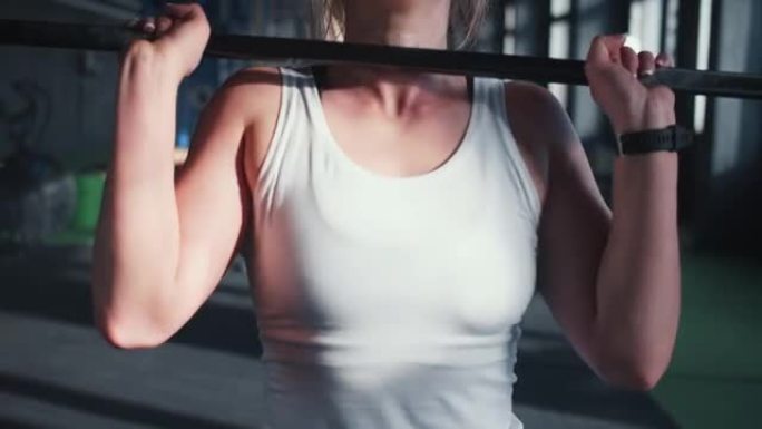 特写美丽的年轻肌肉发达的金发举重运动员女子举起沉重的杠铃，在现代健身房锻炼。