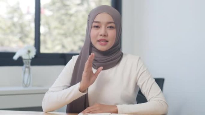 在新的正常办公室里，看着相机的亚洲穆斯林女士与同事谈论视频通话计划。