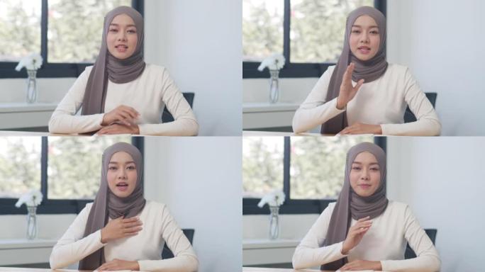 在新的正常办公室里，看着相机的亚洲穆斯林女士与同事谈论视频通话计划。