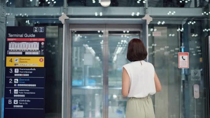 迷人的女人拿着智能手机和护照坐在透明电梯里