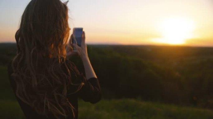 女人在日落时使用移动相机拍照