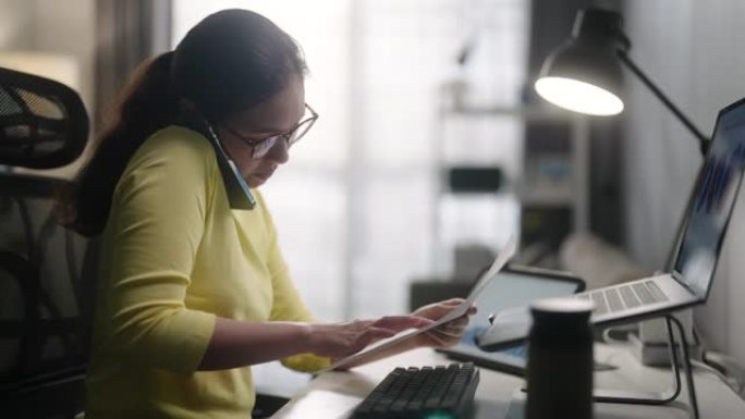 年轻的亚洲妇女在家工作时使用笔记本电脑和手机