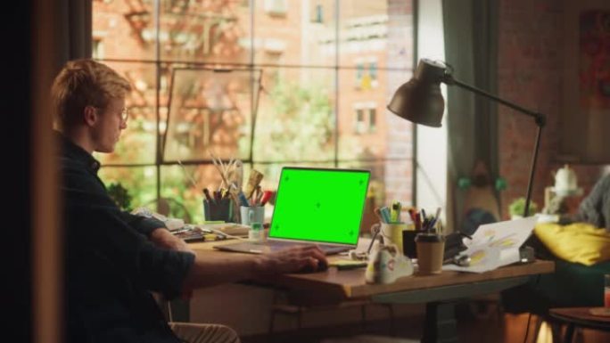在Loft Modern Place从事带有绿屏模型显示的台式计算机的男性专家。十几岁的自由职业者用