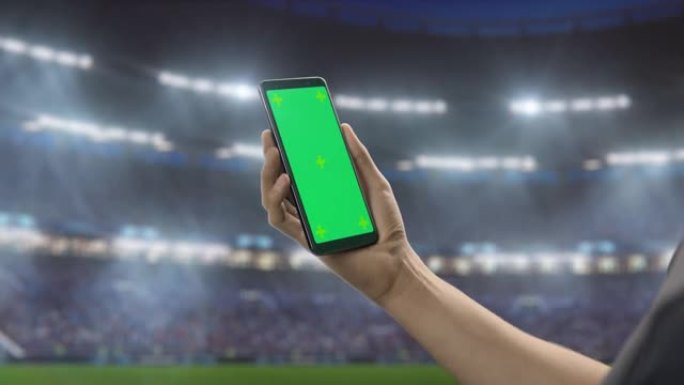 体育场馆锦标赛: 手持绿屏色度键智能手机的人的手。体育赛事，球迷为最喜欢的球队赢得冠军而欢呼。孤立的