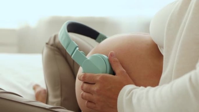 孕妇在肚子上戴耳机，坐在床上休息