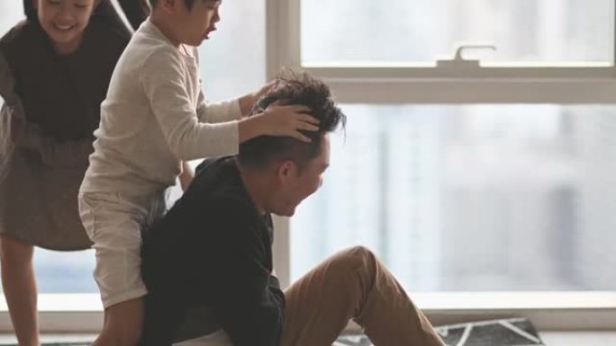 慢动作亚洲华人2父母在客厅里和孩子在家里玩耍，拥抱坐在地上