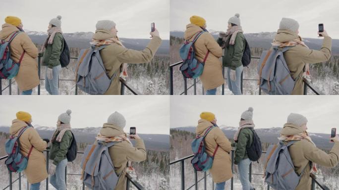 快乐的游客从观景台观看冬季山脉的惊人景观，并使用智能手机拍照