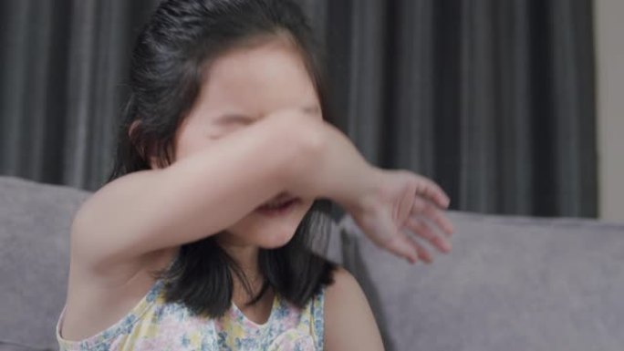 亚洲孩子打喷嚏，用餐巾纸从流感中吹鼻子。她过敏。年轻。在家中患流感的女孩