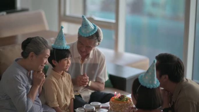 亚洲华人多利一代家庭闭着眼睛在生日蛋糕前做生日祝福在客厅吹生日蜡烛庆祝儿子生日
