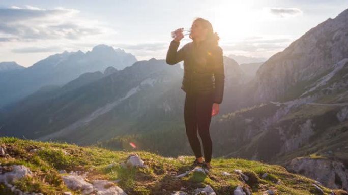 草地上的女人喝水，背景中的山脉全景