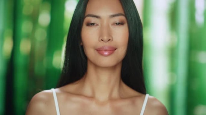 美丽的亚洲女人看着相机，微笑着。女性享受她的美丽、高度自尊、健康。有机化妆品护肤品。抽象绿色森林自然