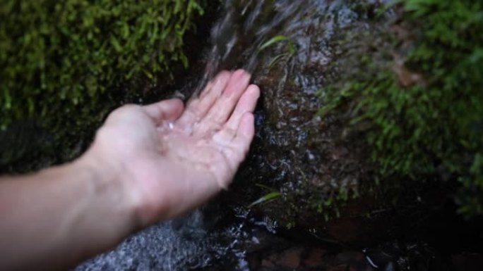 人类的手触摸下降的溪流水