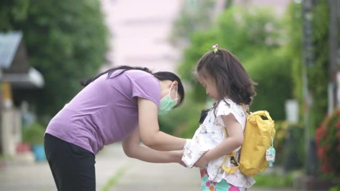 在新型冠状病毒肺炎或冠状病毒大流行时期，母亲正在帮助她在女孩准备上学之前戴上防护口罩