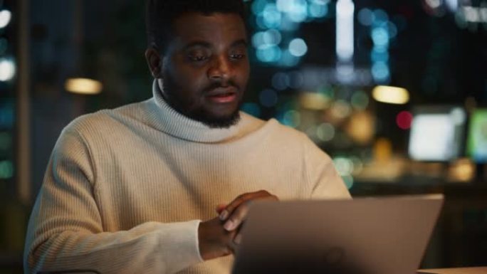 一位英俊的黑人项目经理在夜间办公环境中通过笔记本电脑进行视频通话的肖像。非洲专家通过实时摄像机与营销