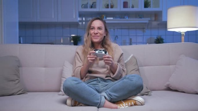 年轻美丽的玩家女孩坐在沙发上，在数字控制台上玩视频游戏的肖像。快乐玩家女人控制视频游戏操纵杆。一个人