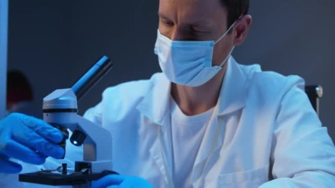 一位穿着实验服的年轻白人科学家在验血时在显微镜下看