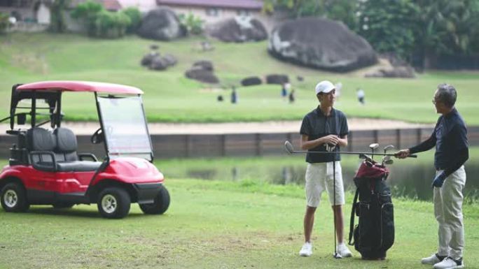 亚洲中国成熟成人从高尔夫球袋中选择驾驶员高尔夫球杆开球，并在高尔夫球场开球点指导他的儿子