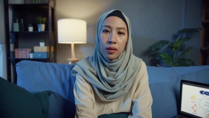 年轻的亚洲穆斯林妇女戴着头巾，心烦意乱的妇女拿着笔记本电脑看相机在线电话会议讨论工作感觉心情不好，员
