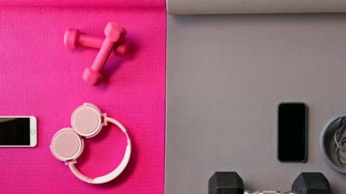 粉色和灰色瑜伽垫，上面装满健身器材。手机、耳机、健身器材、鞋子放在空旷的工作室里。通过有氧运动和举重