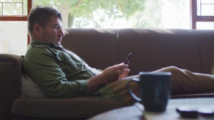 白人男子坐在沙发上，在家中使用智能手机