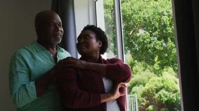 非裔美国老年夫妇在家里看着窗外时互相拥抱