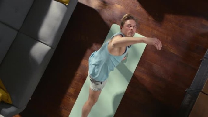 顶视图运动: 漂亮的家伙在家里的运动垫上做瑜伽伸展。肌肉发达，健康，英俊的运动员在他的公寓里做健身锻
