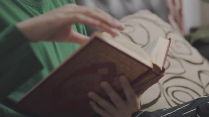 手持视点镜头: 亚洲少女呆在家里读一本模拟书。她翻开学习书的一页。亚洲学生在她家的学校学习历史课作业