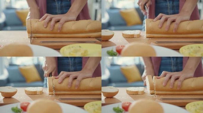 年轻的亚洲女厨师的手拿着刀在家里厨房桌子上的木板上切全麦面包。