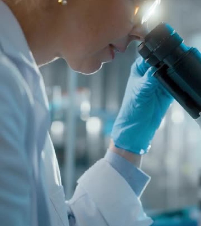 在明亮的医学科学实验室: 戴着眼镜的微生物学家在显微镜下观察分析样品。才华横溢的科学家，与高科技设备