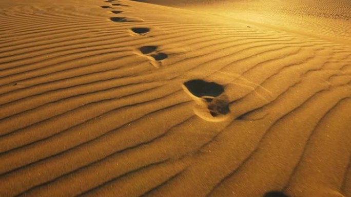 摄像机跟随大沙丘中的脚印。在温暖的日落灯光下，沙漠中的沙子上的脚印。UHD, 4K