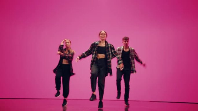 由三个专业舞者组成的多元化小组，在工作室环境中，在带有深粉色背景的大型数字Led墙壁屏幕前表演嘻哈舞