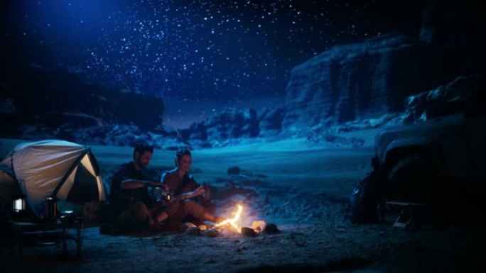幸福的夫妇在峡谷露营，坐在一起看着篝火和星空，她把头靠在他的肩膀上。两个旅行的人在励志度假旅行中惊叹