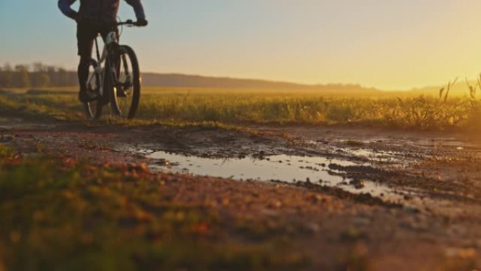 日落时分，SLO MO MTB骑自行车的人在草地之间的小路上穿过泥泞