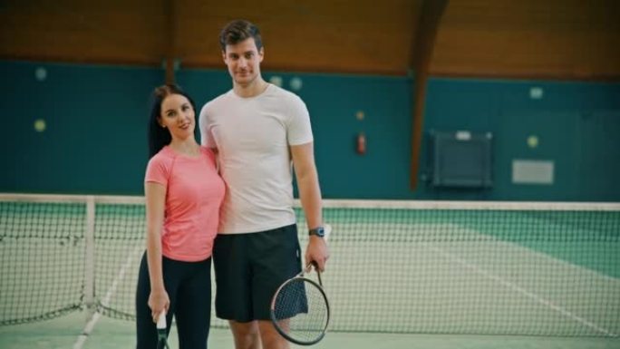 年轻的男教练和女人在网球场上双臂交叉站着