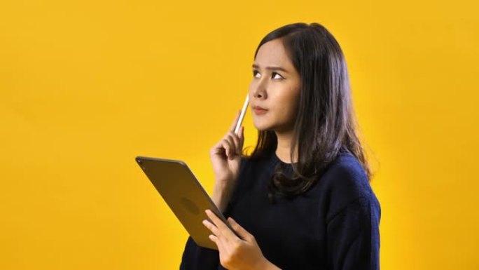 使用隔离在黄色背景上的数字平板电脑拍摄快乐的亚洲女人的肖像