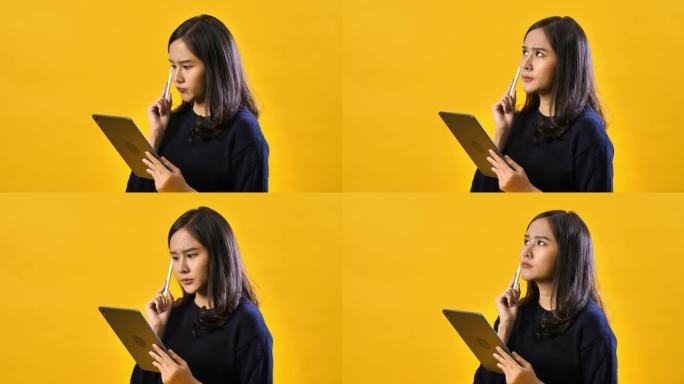 使用隔离在黄色背景上的数字平板电脑拍摄快乐的亚洲女人的肖像