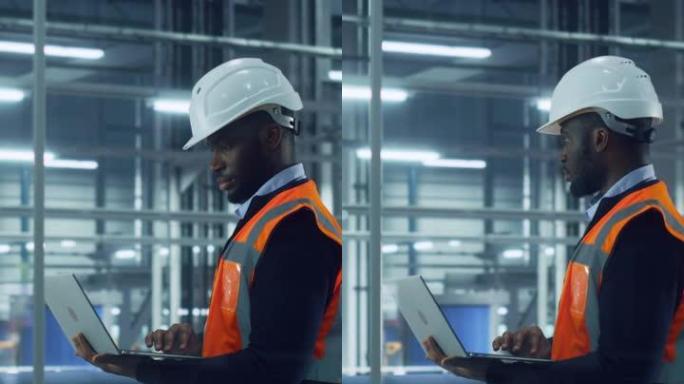 一位非洲裔美国工程师在汽车装配厂办公室使用笔记本电脑的垂直肖像。车辆工厂生产线操作员在计算机上工作，