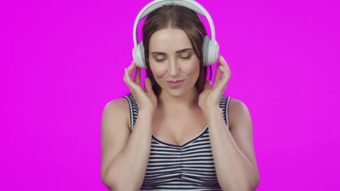4k视频片段，一位迷人的年轻女子使用耳机并在粉红色的工作室背景下跳舞
