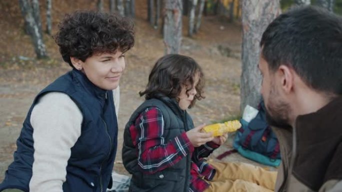 父母在孩子吃玉米在树林里野餐时说话