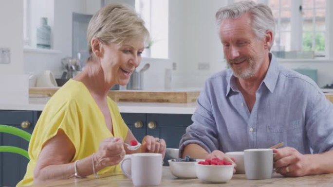 退休夫妇坐在家里的桌子旁，一起吃健康的早餐和新鲜水果