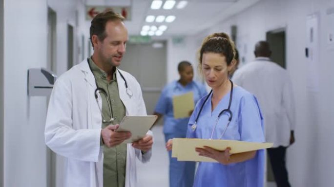 高加索男女医生在医院走廊里聊天，看着平板电脑和病人档案