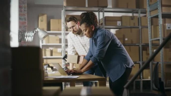多元文化的男性和女性仓库库存经理交谈，使用笔记本电脑并检查零售库存。背景中一排排装满纸箱包装的架子。