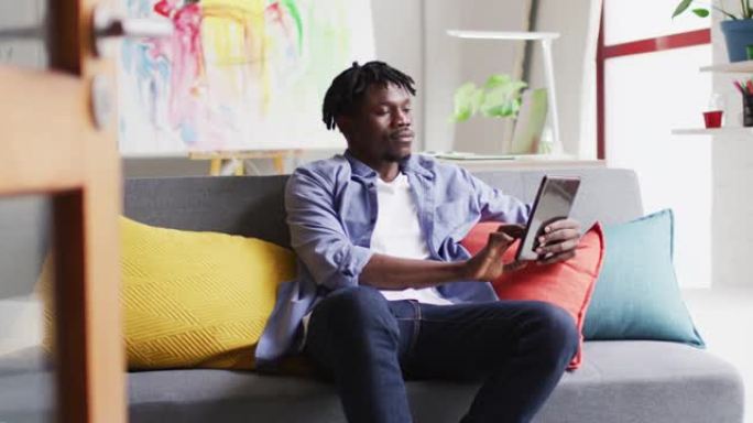 非裔美国男艺术家坐在艺术工作室的沙发上使用数字平板电脑