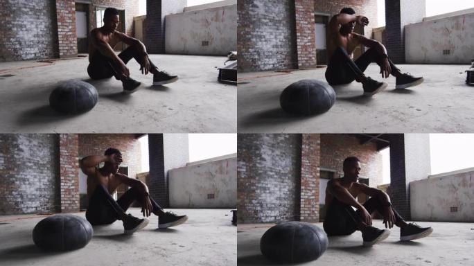 非裔美国男子在空荡荡的城市建筑里用药球锻炼后休息
