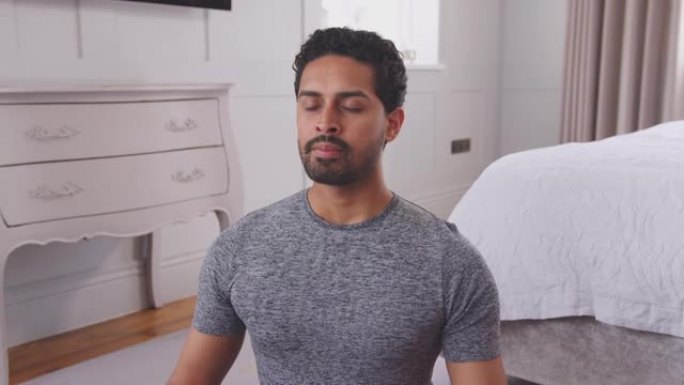 男人穿着健身服坐在家里卧室的地板上做瑜伽