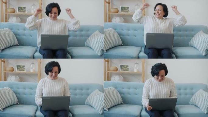 兴奋的女士慢动作用笔记本电脑举起手臂在公寓里享受好消息