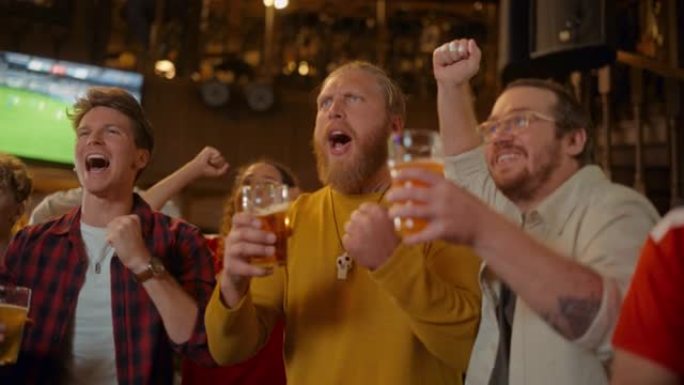 一群足球迷在体育酒吧观看现场足球比赛。三个男性朋友站在电视前，敬酒啤酒杯，庆祝进球和冠军获胜。