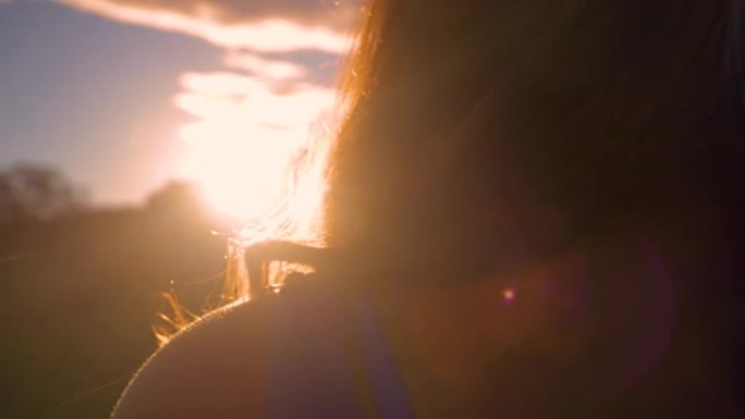 特写镜头，镜头闪耀着棕色长波浪头发的年轻女士走向日落