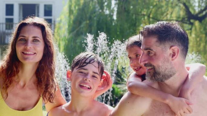 穿着游泳衣的家庭肖像在花园洒水车的水中玩耍